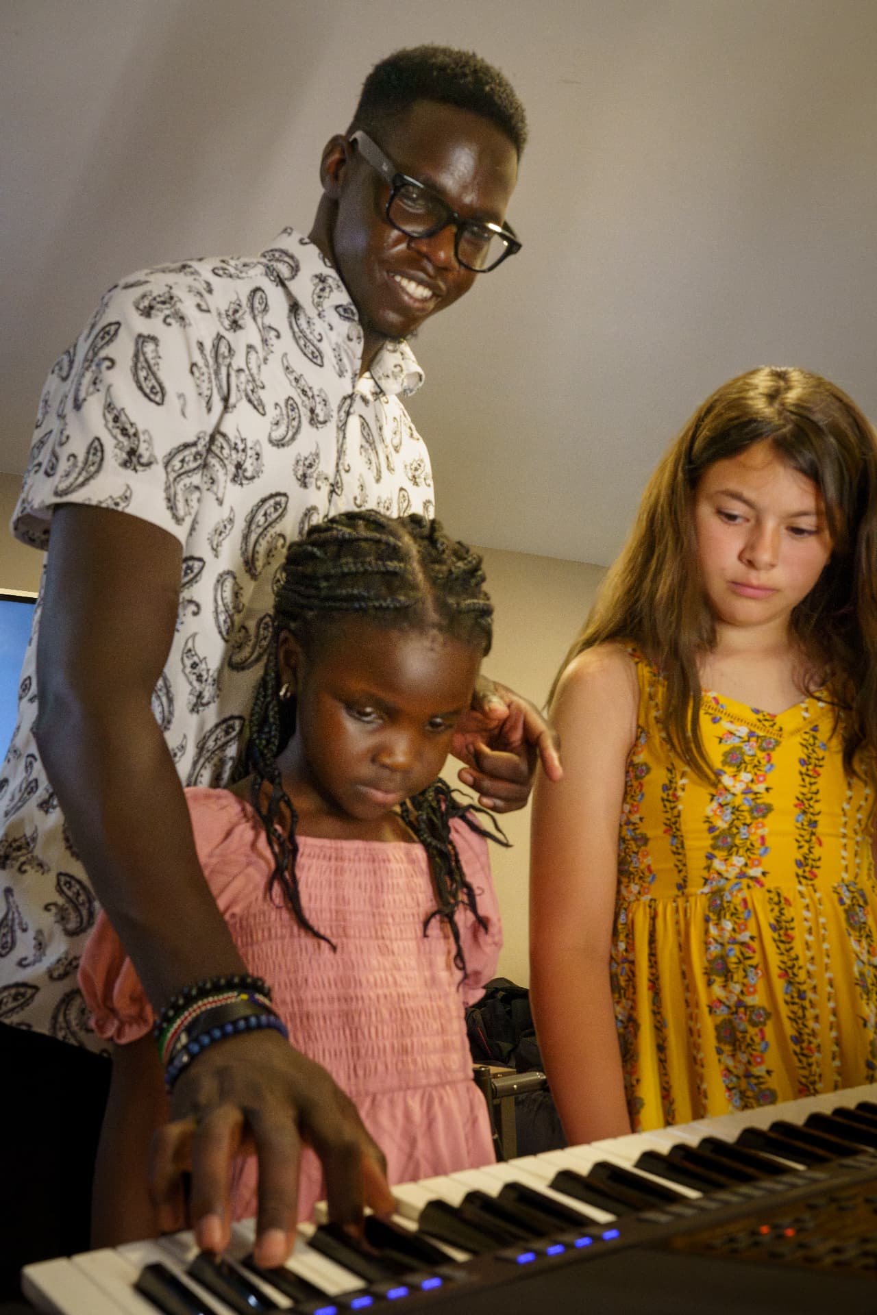 Peace Academy instructor teaching two students at the piano keyboard